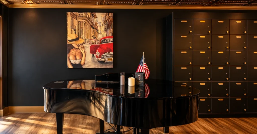 Black baby grand piano beneath a Havana painting beside Jallo’s cigar lockers.
